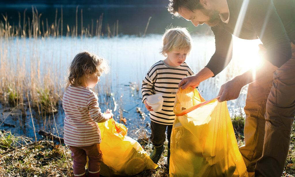 Vater sammelt mit seinen kleinen Kindern Müll im Freien