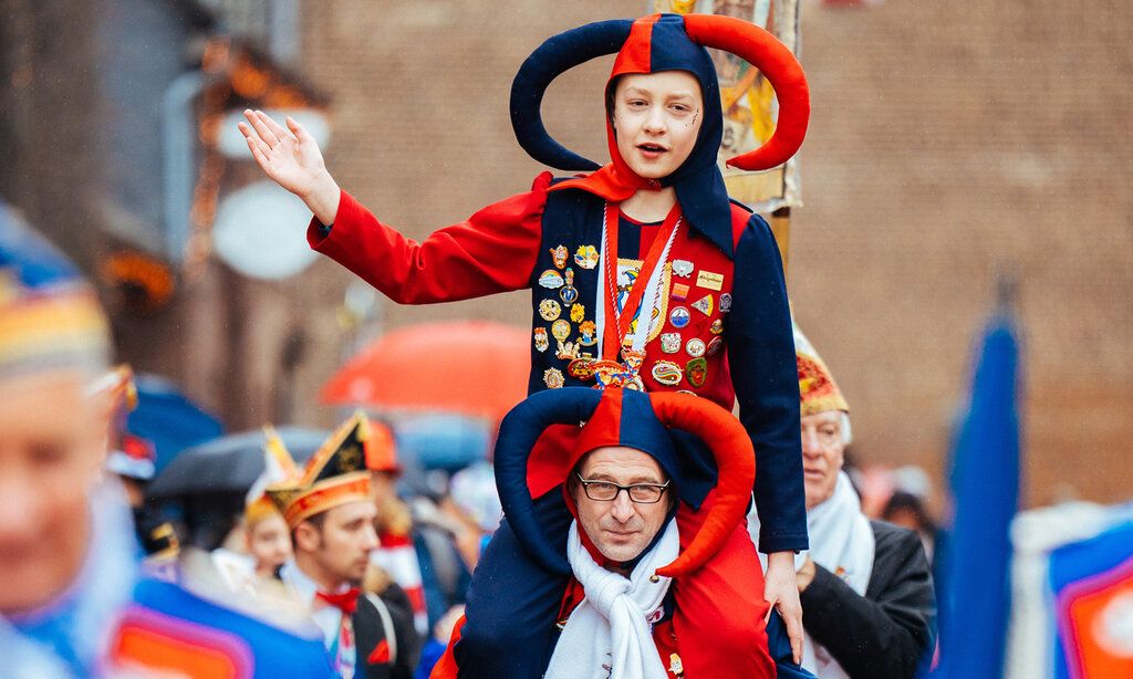 Als Narr erkleideter Vater trägt verkleideten Sohn beim Monheimer Karneval Huckepack