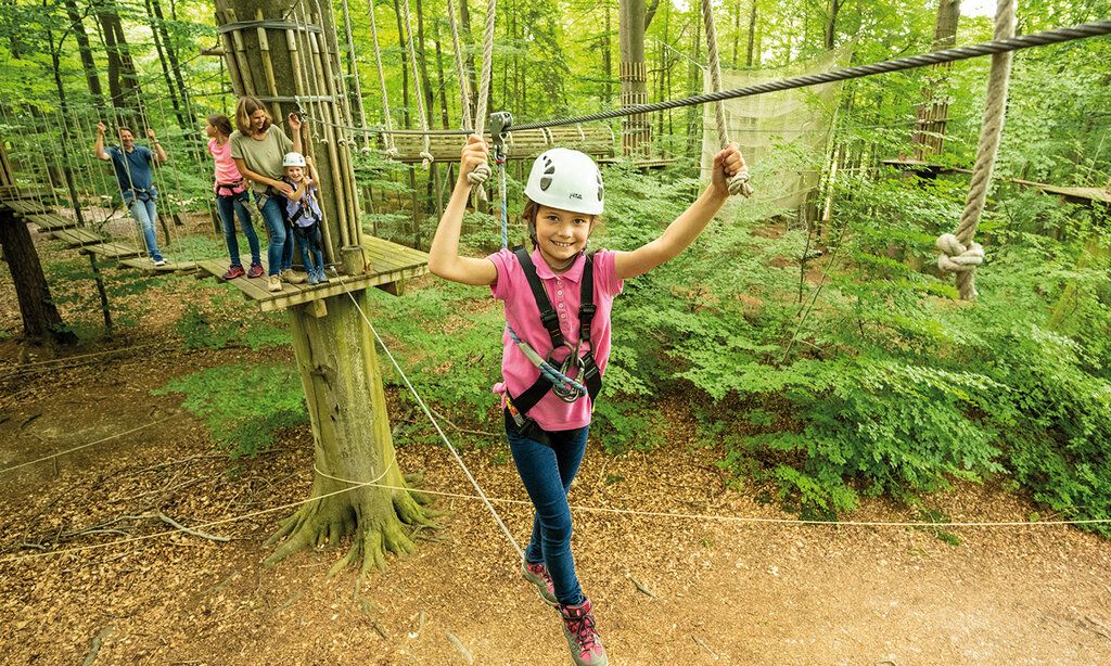 Mädchen mit Helm klettert im Hochseilgarten im Wald