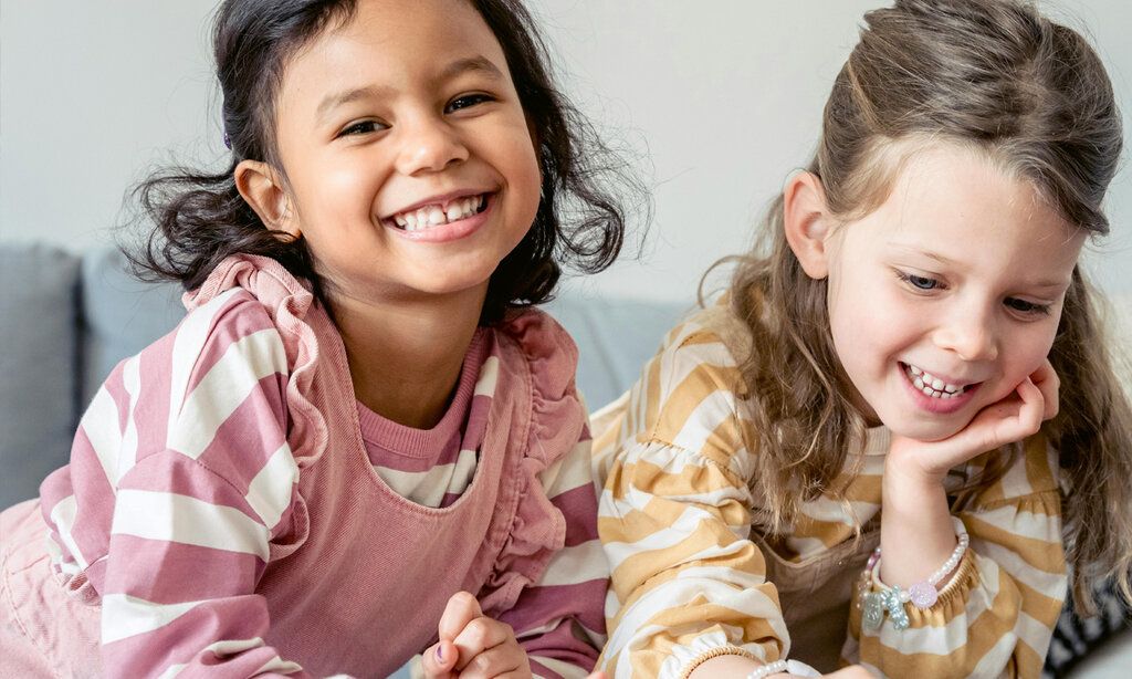 Zwei Mädchen sitzen nebeneinander und lachen