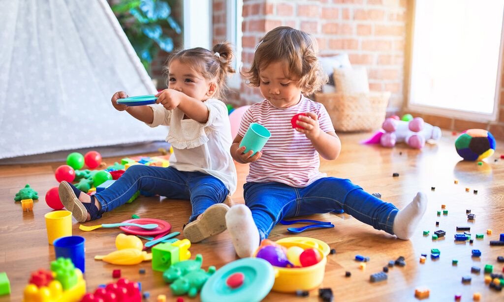 Zwei Mädchen sitzen auf dem Fußboden und spielen mit buntem Spielzeug