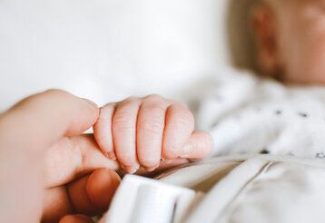 die Hand eines Babys umfasst den Zeigefinger der Mutter