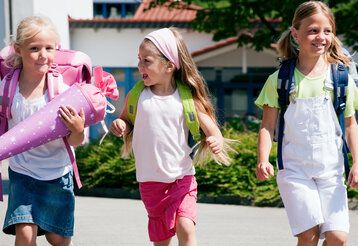 Drei Mädchen laufen nebeneinander her, das Mädchen links trägt eine Schultüte