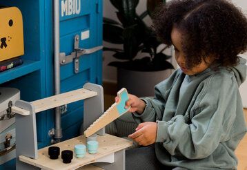 Mädchen spielt mit einer Spielzeug-Säge an einer Spielzeug-Werkbank