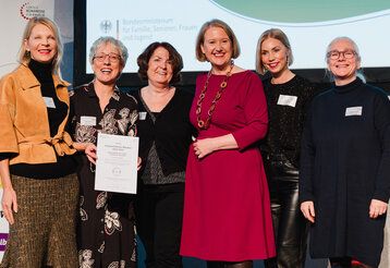 Gruppenbild Bündnisdialog, sechs Frauen auf einer Bühne, eine hält eine Urkunde