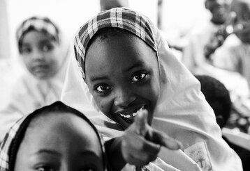 Mädchen schaut in die Kamera und zeigt mit dem Finger