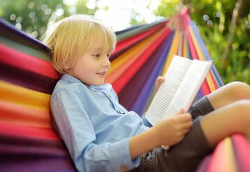 ein Junge liegt in einer bunt gestreiften Hängematte und liest ein Buch