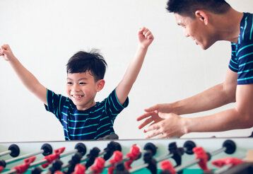 kleiner Junge steht mit seinem Vater an einem Tischfußball und jubelt