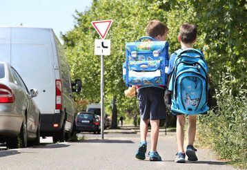 Zwei Jungs von hinten mit Schulrucksäcken gehen nebeneinander auf einem Bürgersteig