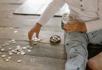 ein Kind sitzt auf dem Boden und sammelt Münzen im Glas