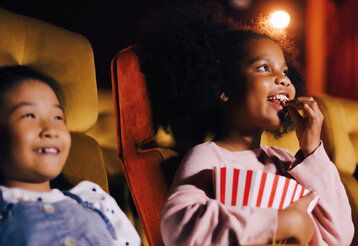 zwei Kinder sitzen im Kinosaal, ein Mädchen isst Popcorn