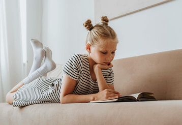 ein Mädchen liegt bäuchlings auf einem Sofa und liest in einem Buch