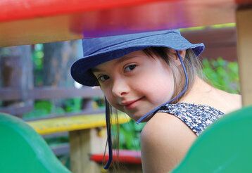 Porträt, Mädchen mit Down Syndrom guckt durch ein Klettergerüst auf einem Spielplatz