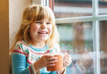 Mädchen sitzt mit Tasse am Fenster und lacht