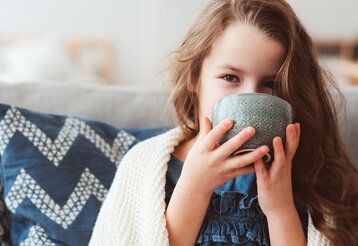 Mädchen sitzt auf einem Sofa und trinkt aus einer Tasse