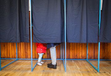 Menschen wählen in Wahlkabine mit Kind