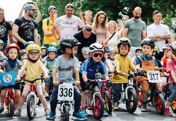 eine Gruppe von Kleinkindern steht mit Laufrädern am Start für ein Laufrad-Rennen, im Hintergrund die Eltern