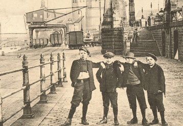 historisches Foto von 4 Jungen auf der unteren Rheinwerft; im Hintergrund Hafenbetrieb; Pegeluhr; Schlossturm