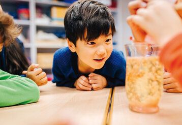 Kinder schauen auf ein Glas, in dem ein Experiment stattfindet