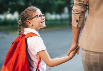 Tochter und Mutter gehen Hand in Hand, die Tochter schaut hoch zur Mutter, die ist aber nur im Anschnitt zu sehen