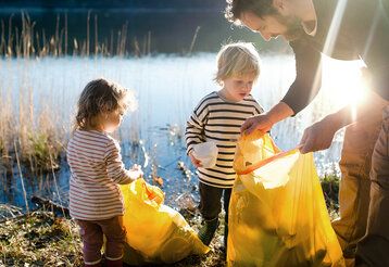 Vater sammelt mit seinen kleinen Kindern Müll im Freien