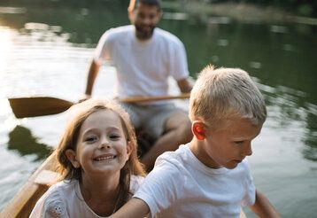 Vater mit Sohn und Tochter auf einem kleinen Fluss im Paddelboot, Abendstimmung
