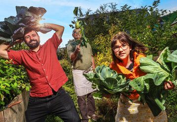 zwei Männer und eine Frau mit Gemüse im Hochbeetgarten