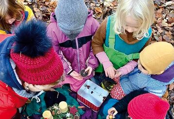 Kinder von oben fotografiert, die im Laub sitzen, in der Mitte eine Keksdose und ein Adventskranz