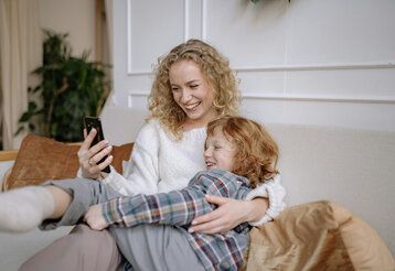 Mutter und Sohn auf dem Sofa schauen gemeinsam auf das Smartphone