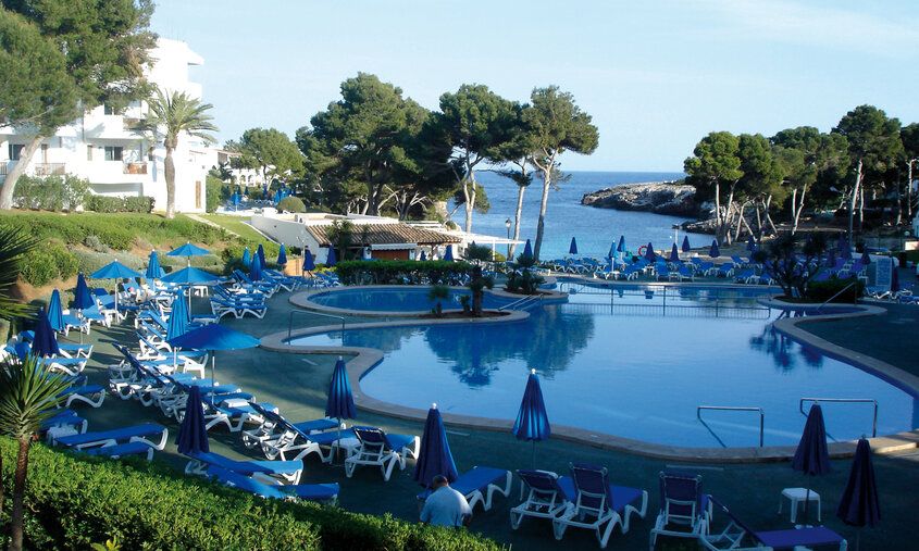 Poolanlage eines Familienhotels auf einer spanischen Insel, im Hintergrund Meer